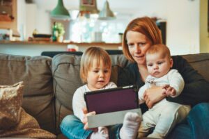 woman with small children on lap look at tablet computer